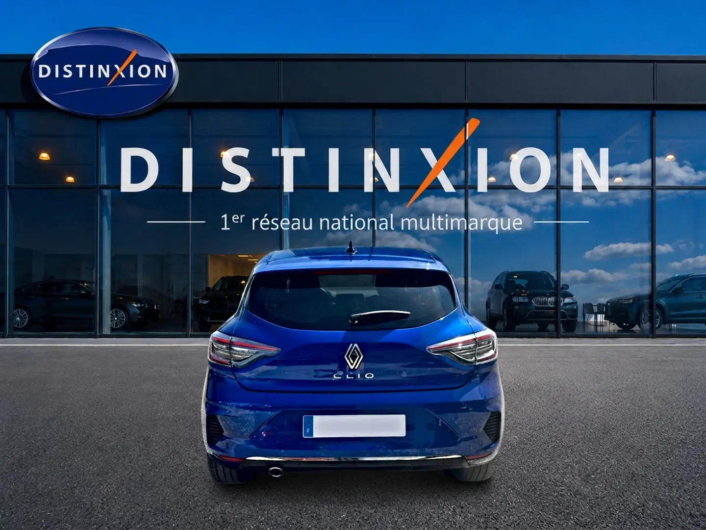 Vue arrière d'une Renault Clio V bleu iron garée devant une vitrine avec logo Distinxion.