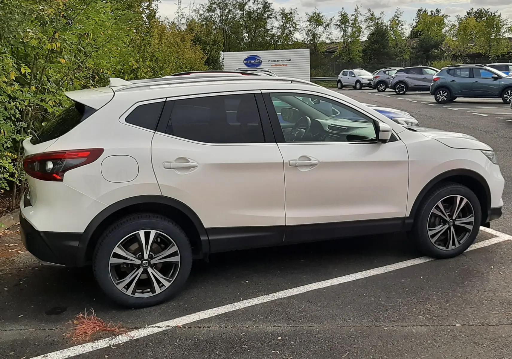 Vue de profil côté droit d'un Nissan Qashqai blanc 2018 avec jantes alliage bicolores sur un parking extérieur.