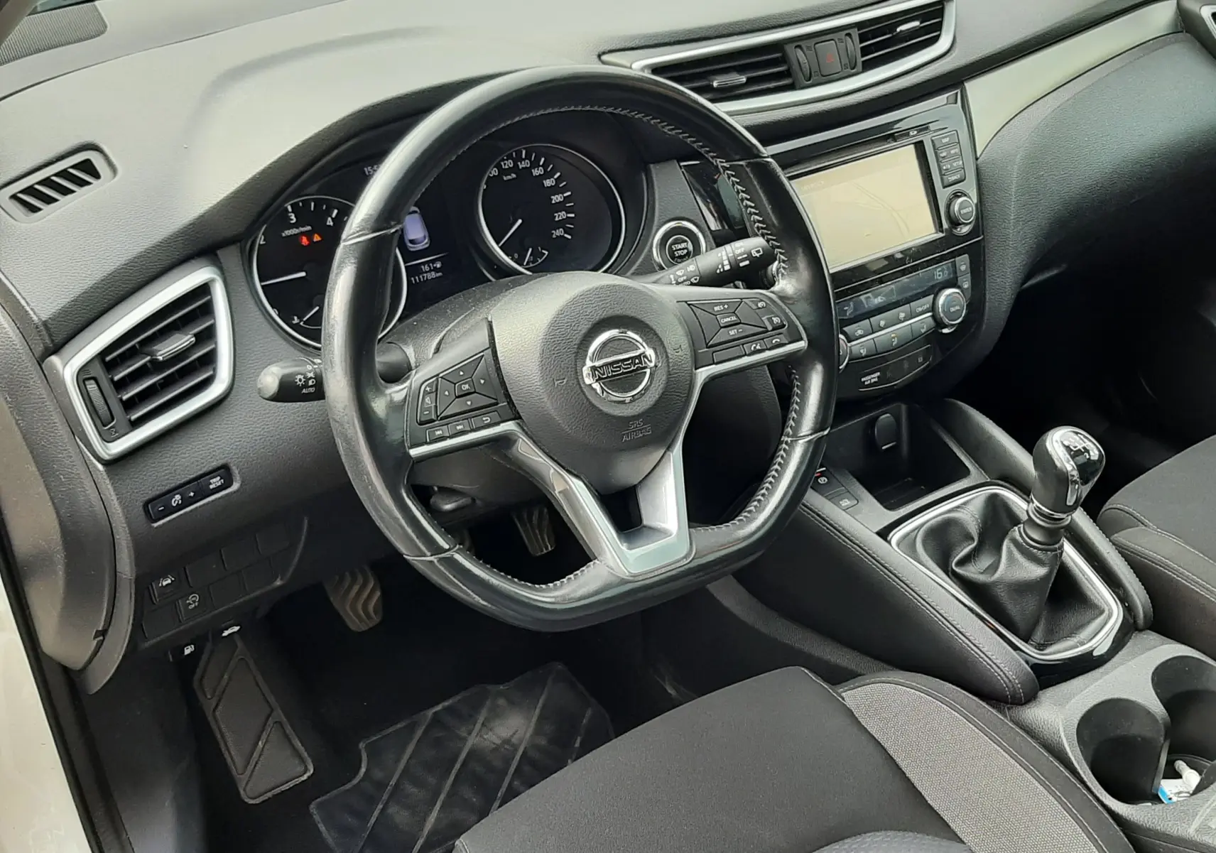 Vue intérieure côté conducteur du Nissan Qashqai 1.5 DCI 115ch N-Connecta 2018, volant cuir, boîte manuelle et tableau de bord noir.