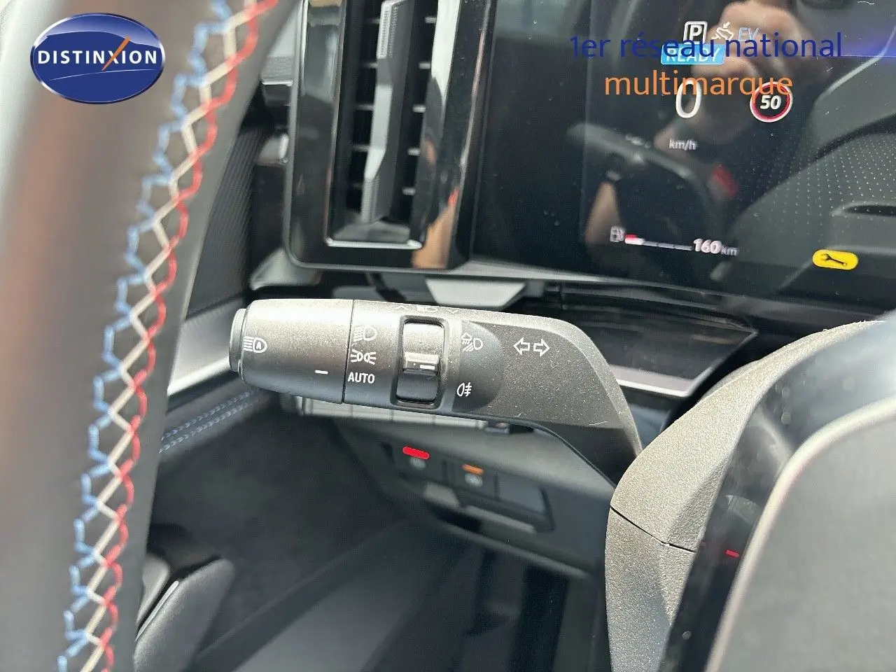 Gros plan sur la commande des phares et clignotants du Renault Austral 2024 bleu iron metal avec volant surpiqué tricolore.