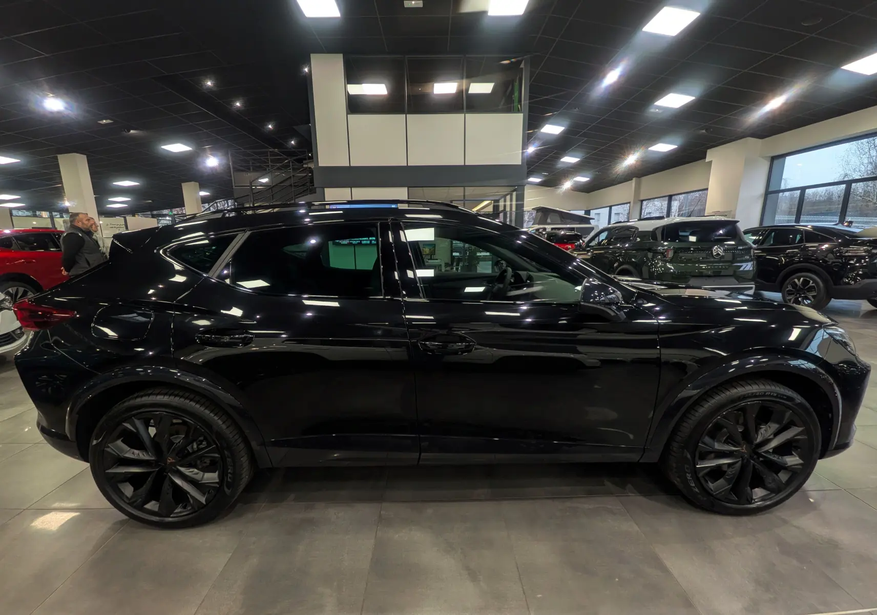 Vue de profil côté gauche d'une CUPRA Formentor eHybrid 2025 en noir minuit avec jantes noires et toit ouvrant en showroom.