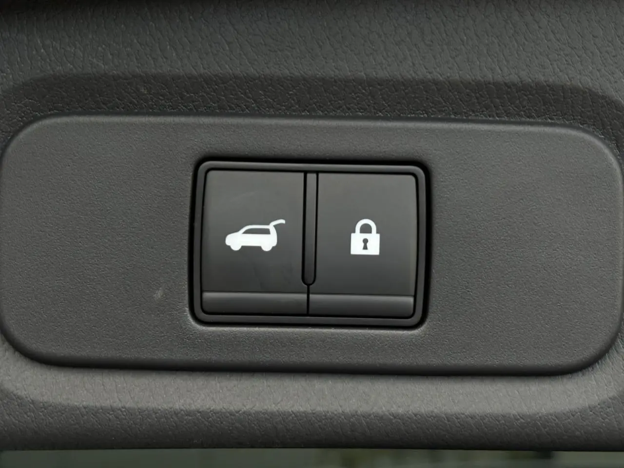 Gros plan sur les boutons de hayon électrique et de verrouillage intérieur, tableau de bord noir du Nissan Qashqai gris Ceramic.