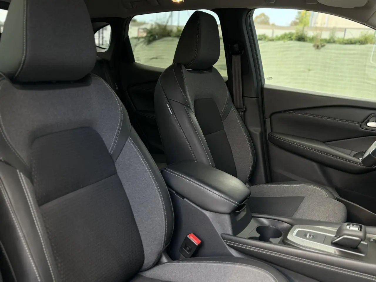 Vue intérieure côté droit des sièges avant gris et noir du Nissan Qashqai 2025 avec accoudoir central et console de boîte automatique.