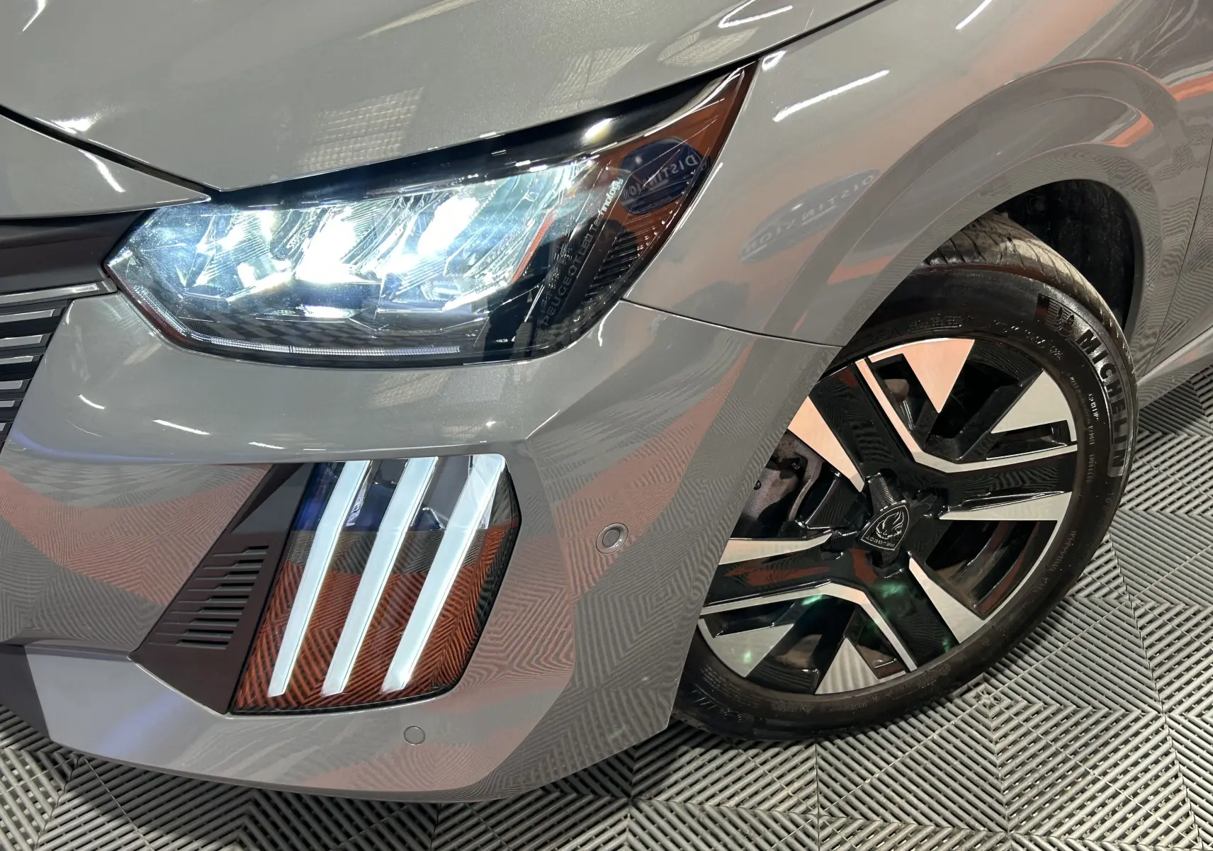 Gros plan sur l'avant droit gris Selenium de la Peugeot 208 2025, mettant en valeur le phare LED et la jante alliage noire et argent.