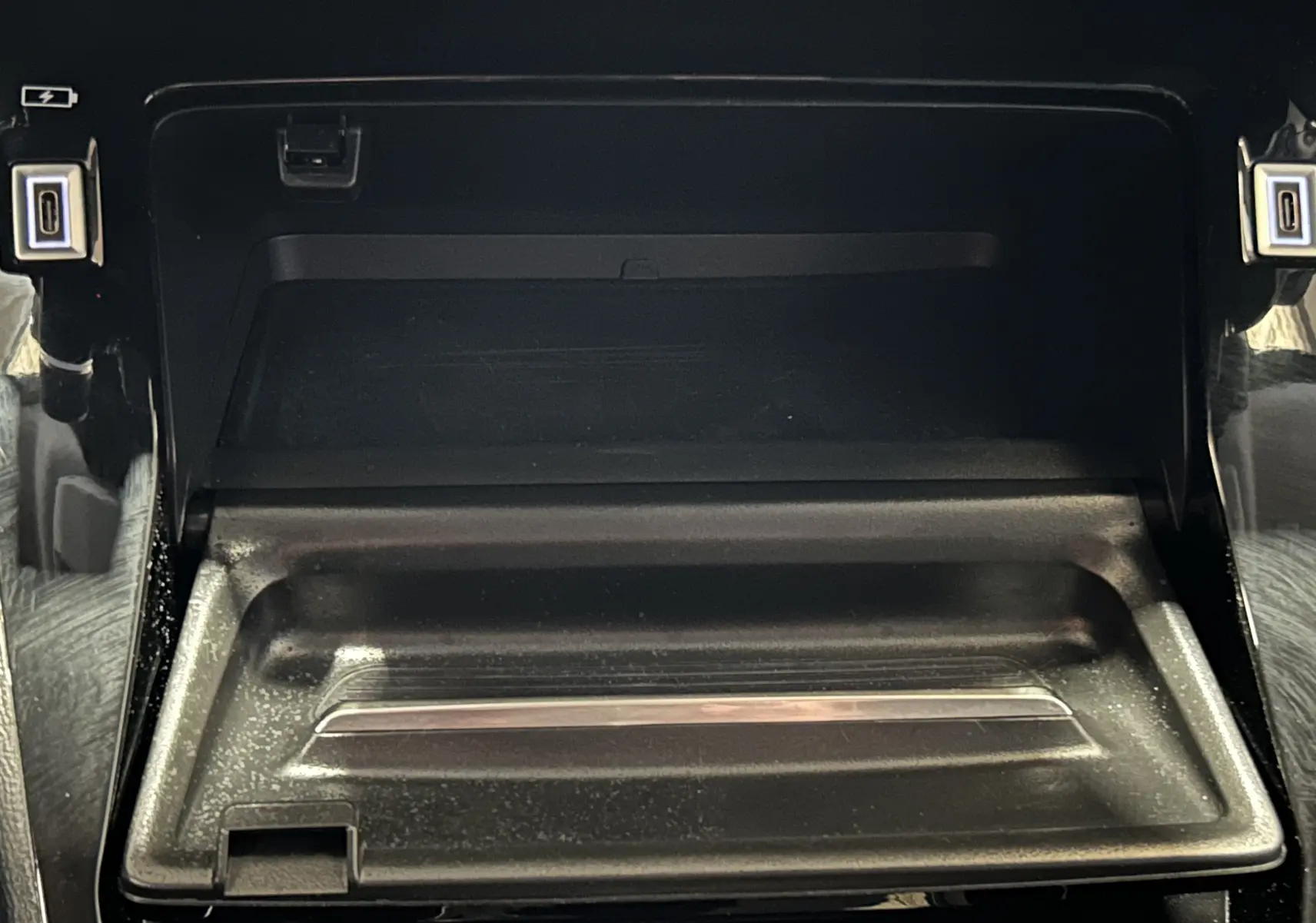 Détail du compartiment de rangement central avant de la Peugeot 208 Turbo 100 BVM6 Allure, finition noire brillante.