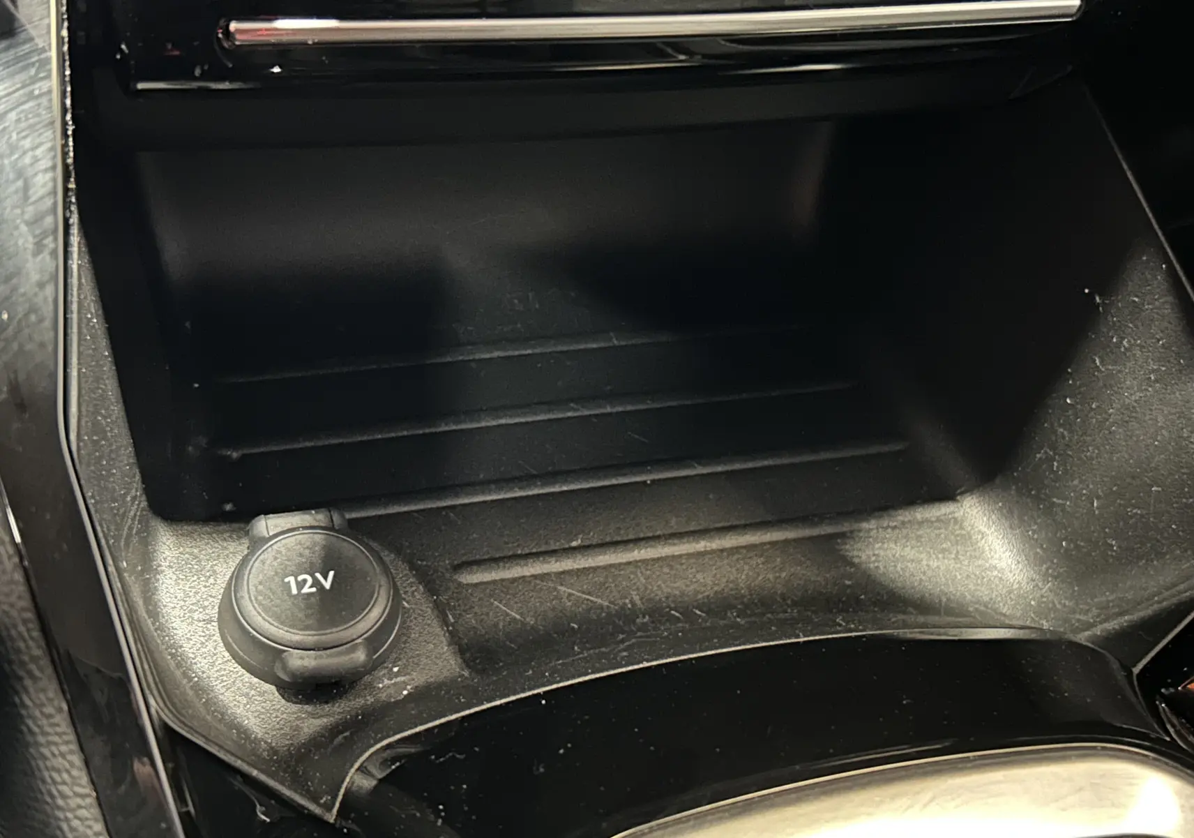 Prise 12V en gros plan dans la console centrale noire de la Peugeot 208 Turbo 100 BVM6 Allure gris Selenium.