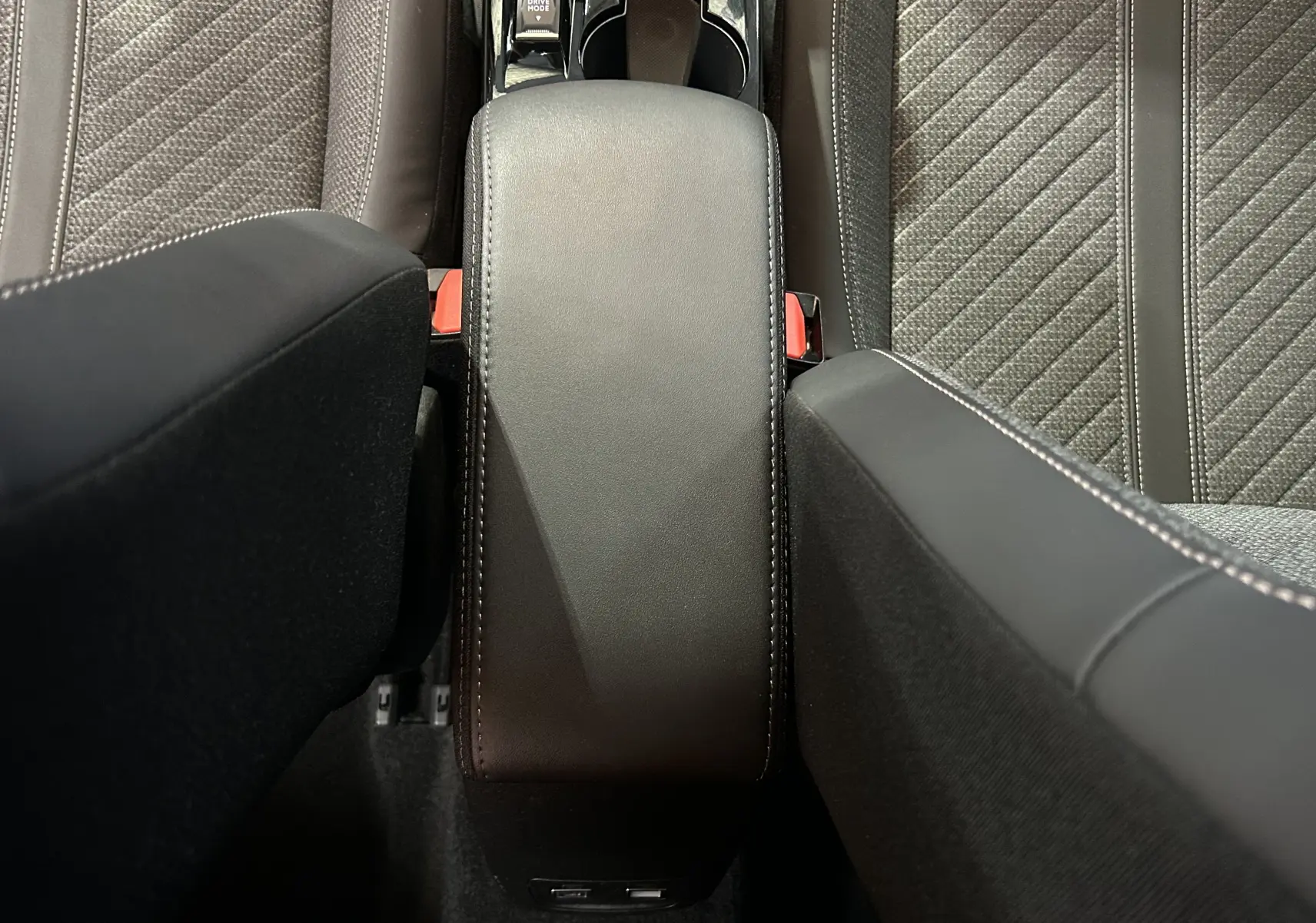 Vue plongeante sur l'accoudoir central en cuir noir et les sièges tissu gris de la Peugeot 208 Turbo 100 BVM6 Allure.