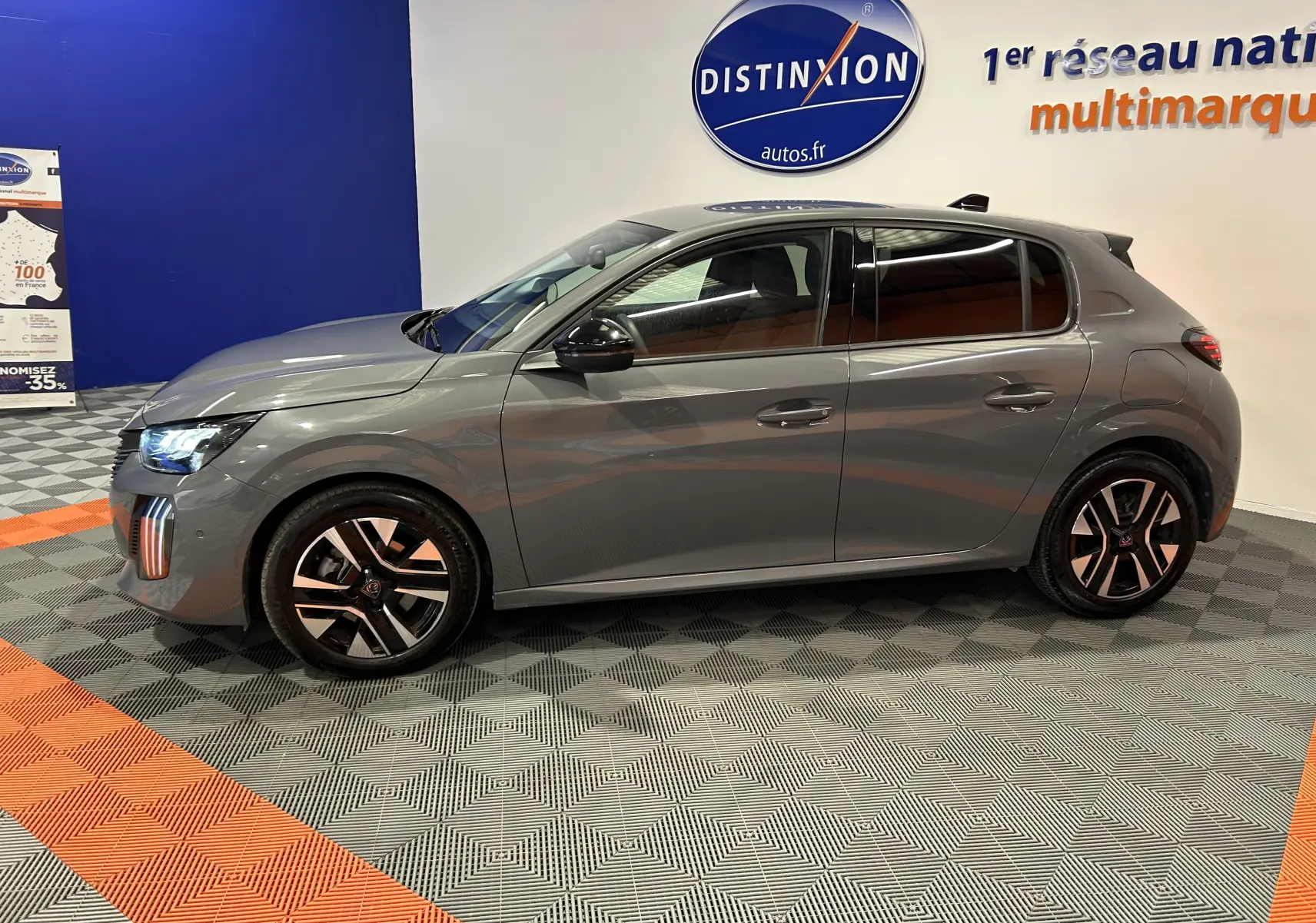 Peugeot 208 gris Selenium vue de profil côté gauche, avec jantes alliage et feux avant allumés en intérieur showroom.