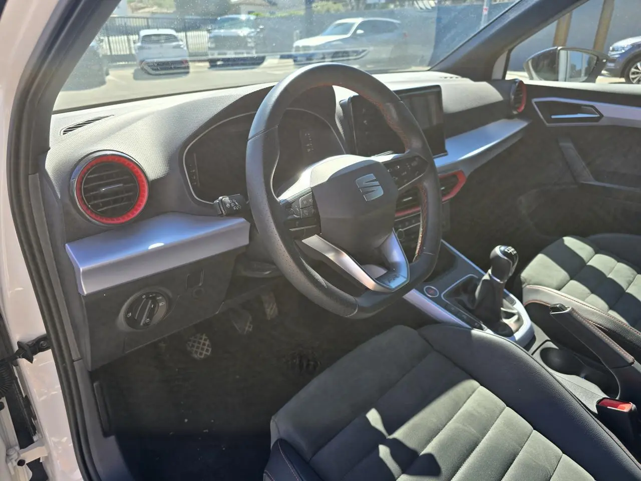 Vue intérieure côté conducteur du SEAT Arona 2024, volant sport cuir noir avec surpiqûres rouges et sellerie suédine noire.