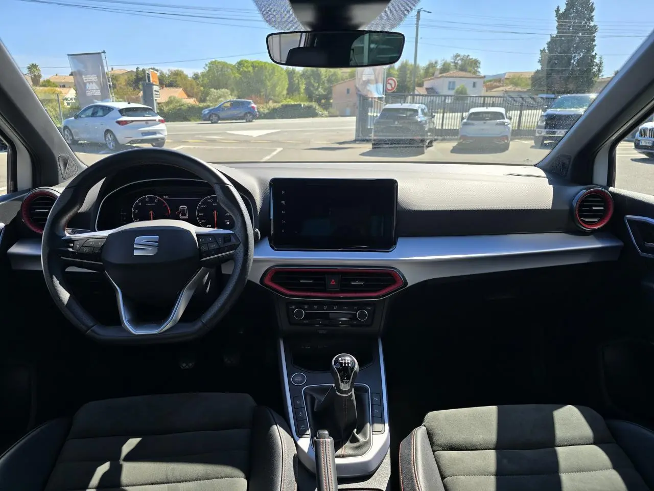 Vue intérieure frontale du tableau de bord du SEAT Arona 2024, volant cuir noir, détails rouges et écran tactile central.