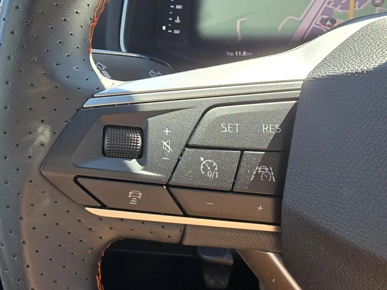 Gros plan sur les commandes du volant en cuir perforé noir avec surpiqûres rouges du SEAT Arona 2024, mode régulateur et aide à la conduite.