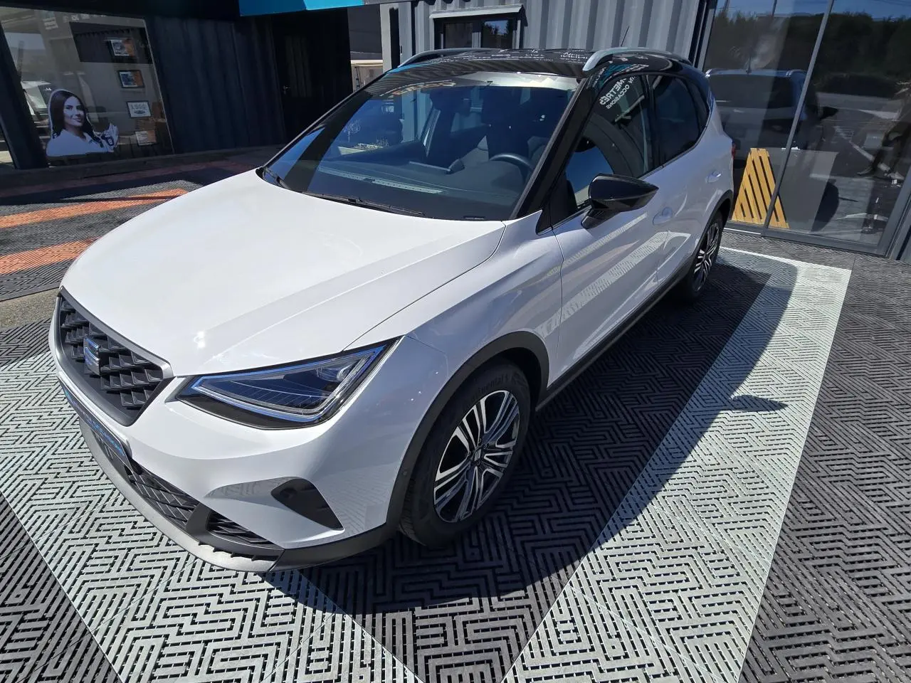 Vue 3/4 avant droite d'une SEAT Arona 2024 blanche avec toit noir et jantes alliage distinctives.