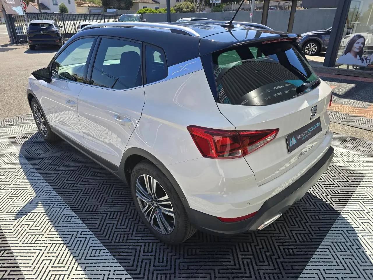 Vue 3/4 arrière droite d'un SEAT Arona blanc avec toit noir et jantes alliage, stationné en extérieur au soleil.