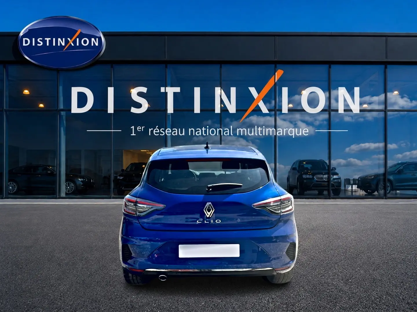 Vue arrière d'une Renault Clio V bleu iron garée devant une vitrine avec logo Distinxion visible.