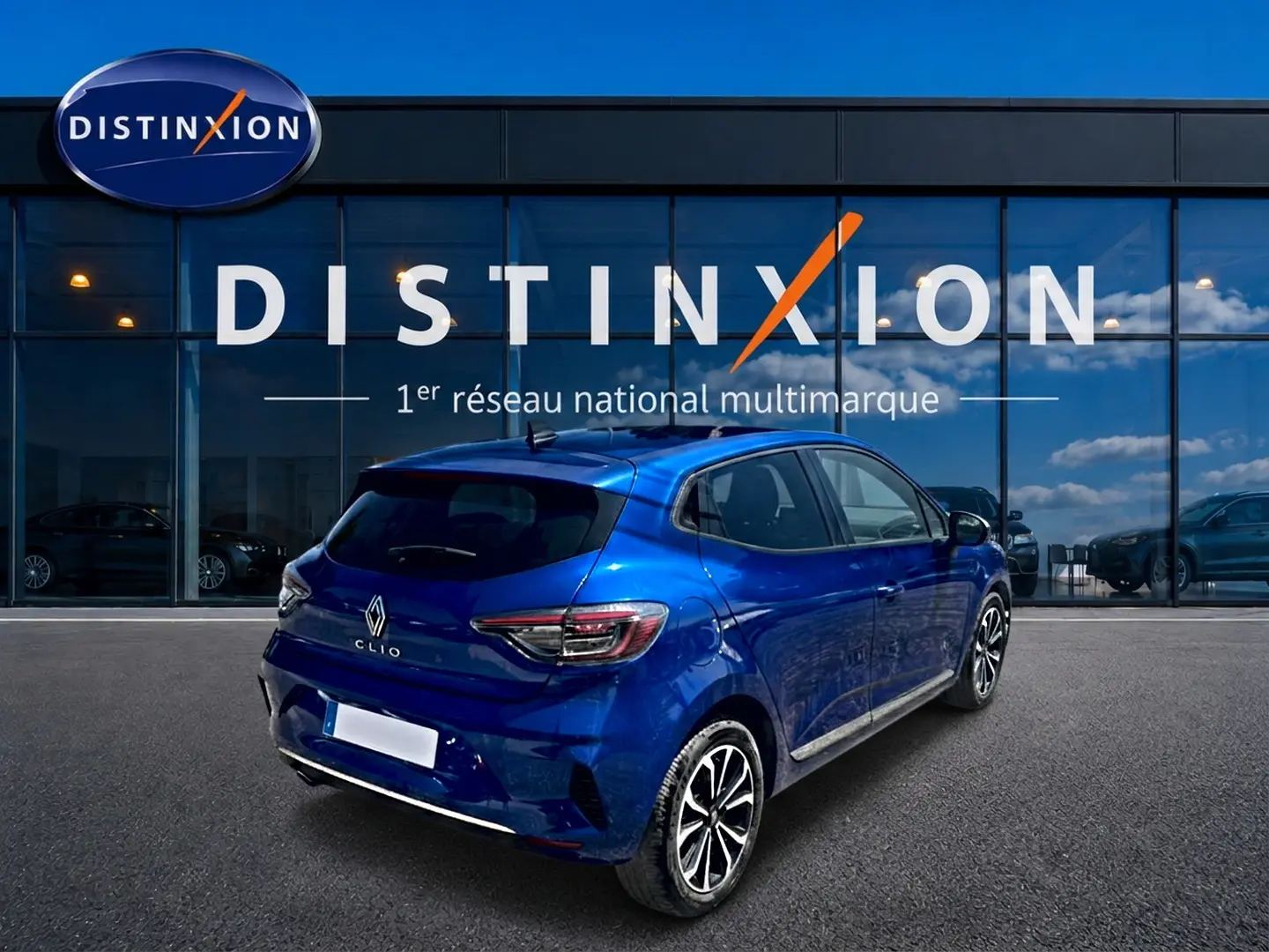 Renault Clio V bleu iron vue 3/4 arrière droit, avec jantes alu et becquet arrière visible devant vitrine Distinxion.