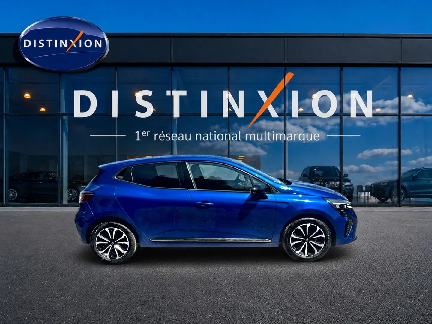 Profil droit d'une Renault Clio V bleu iron 2025 avec jantes alliage et poignées ton carrosserie devant un showroom Distinxion.