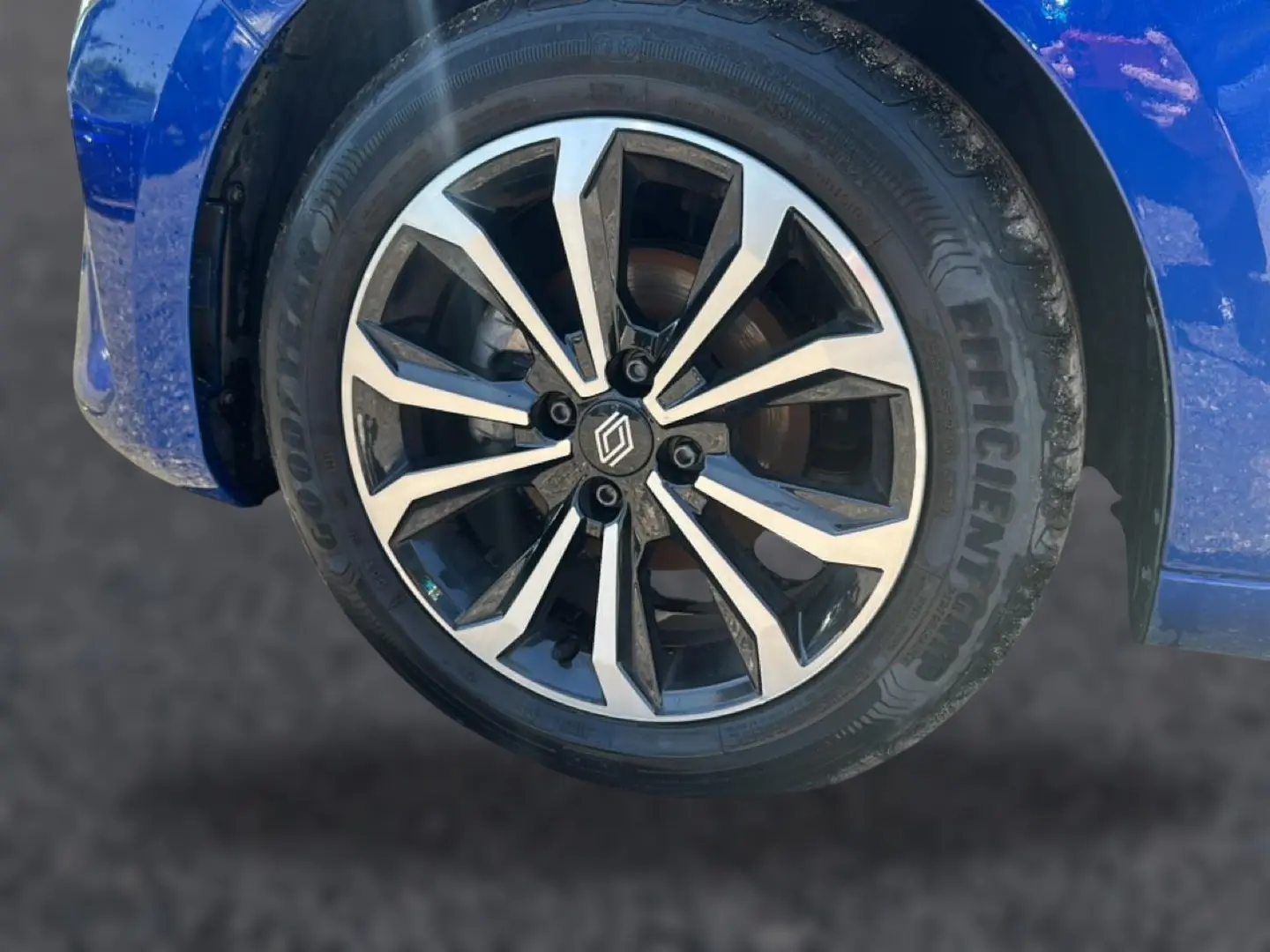 Gros plan sur la roue avant gauche avec jante alu bicolore et partie de la carrosserie bleu iron de la Renault Clio V.
