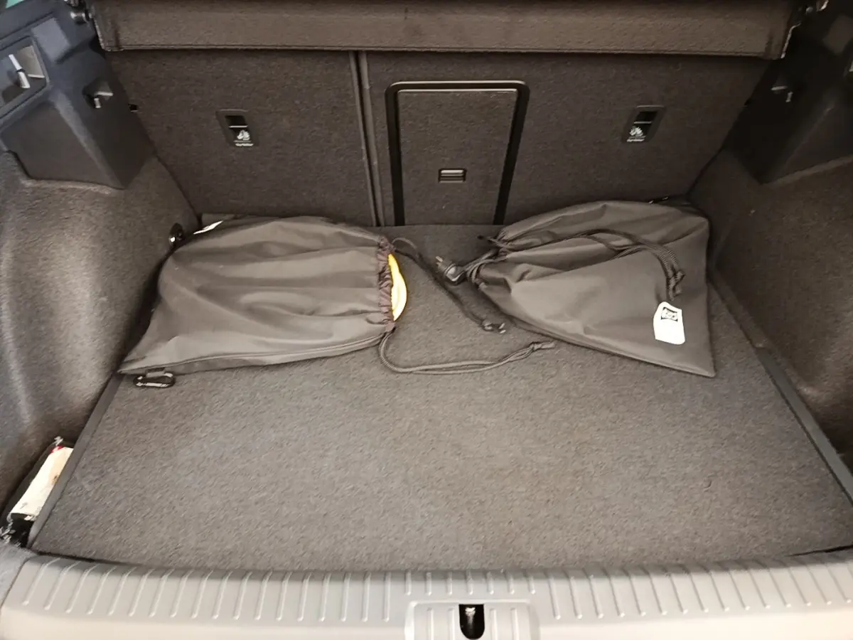 Vue intérieure du coffre du CUPRA Formentor 1.4 e-HYBRID 2024 avec tapis gris et deux sacs noirs posés.