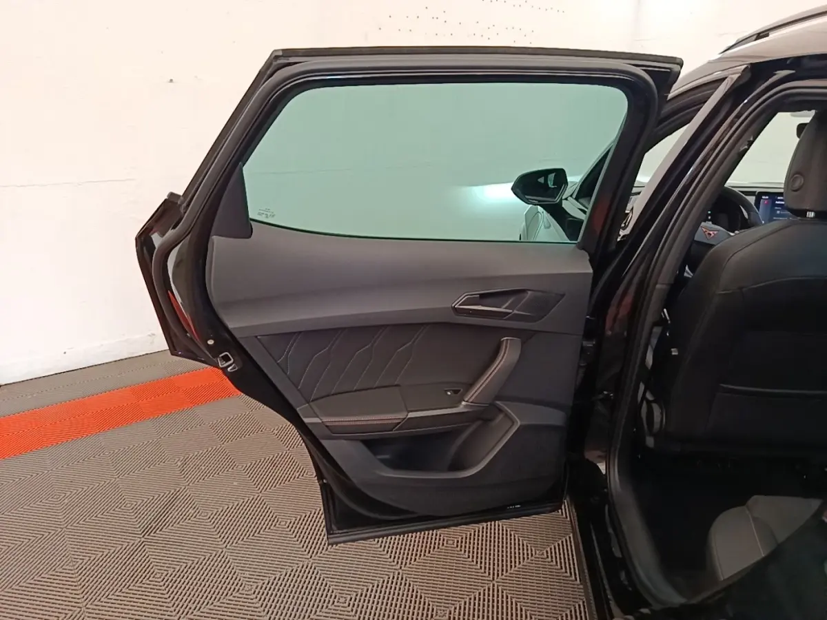 Vue intérieure de la porte arrière gauche ouverte d’un CUPRA Formentor noir, avec sellerie et garnitures sombres.