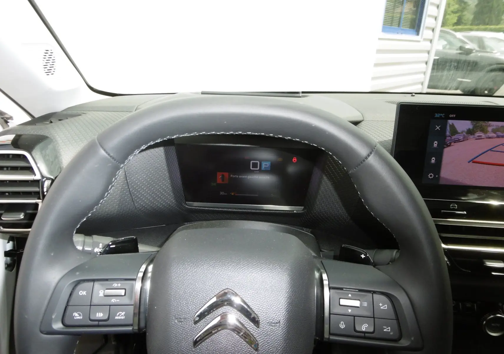 Vue rapprochée du volant et du tableau de bord numérique d'une Citroën C4 X blanche, avec écran multimédia affichant la caméra de recul.