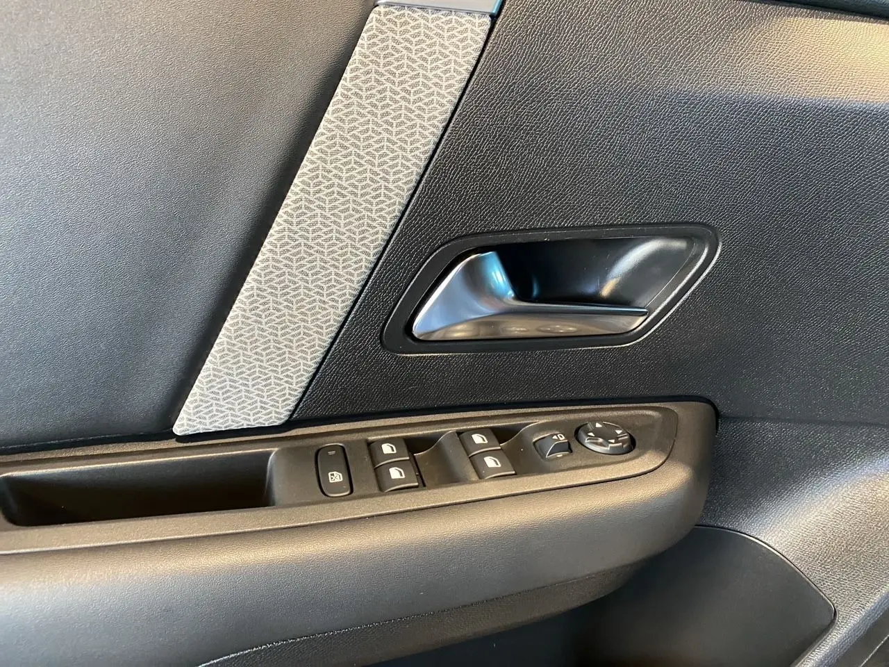 Détail de la porte côté conducteur de la Citroën C4 2023, avec commandes de vitres et poignée argentée sur panneau noir et gris.