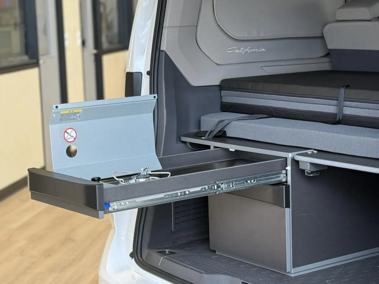 Vue arrière droite du Volkswagen California blanc Candy montrant la mini-cuisine coulissante et la banquette intérieure.