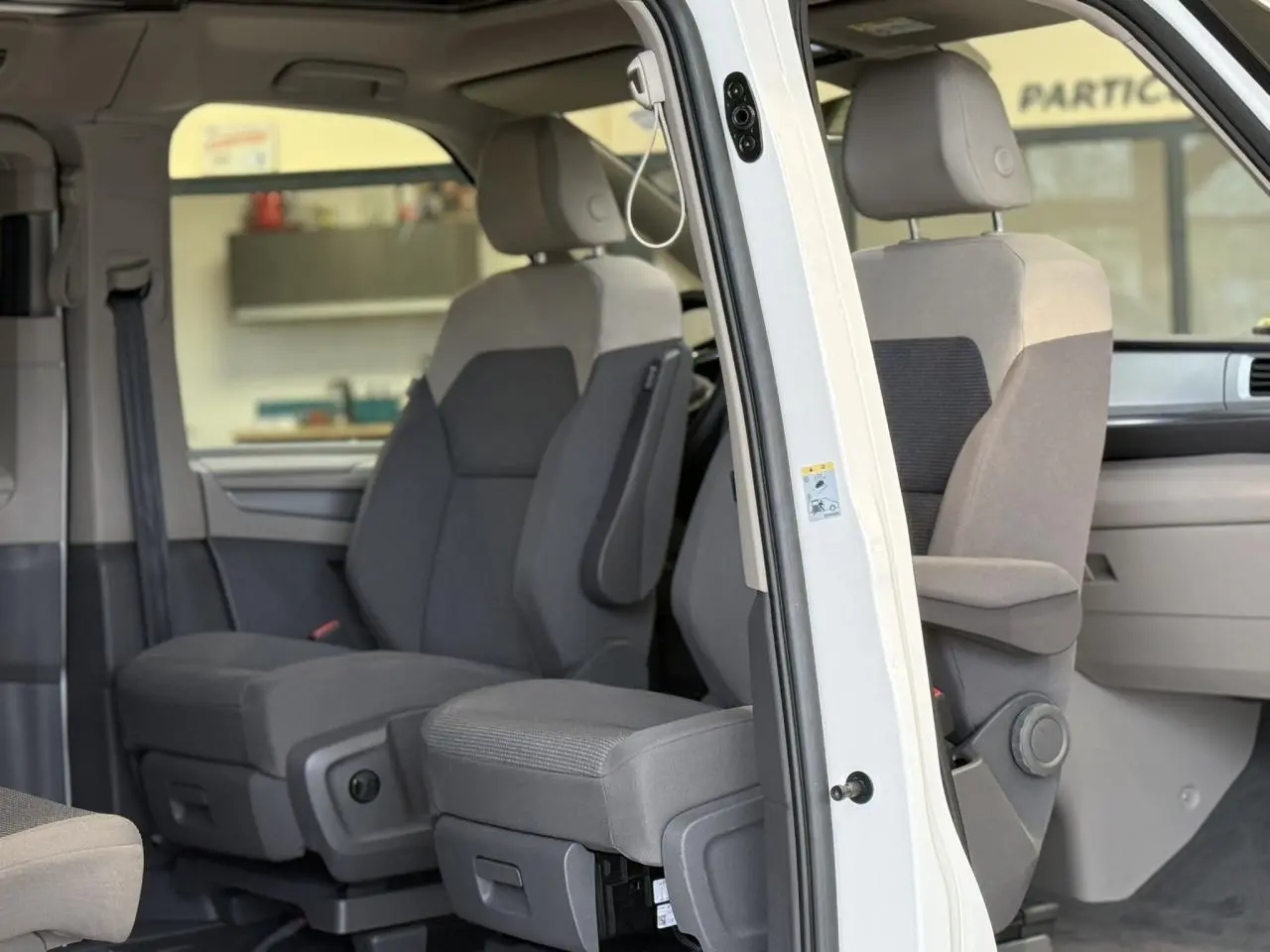 Vue intérieure côté droit du Volkswagen California T7 blanc Candy, montrant les sièges avant avec accoudoirs et appuis-tête.