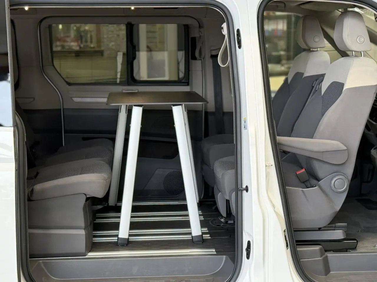 Vue latérale droite du Volkswagen California T7 blanc Candy, porte coulissante ouverte sur l'intérieur avec table repliable entre les sièges.