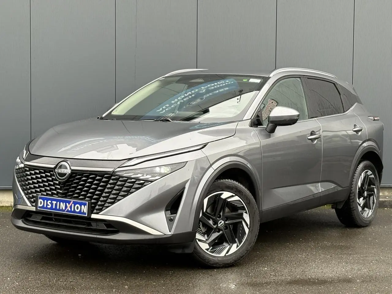 Vue 3/4 avant droite du Nissan Qashqai 2024 gris Squale avec jantes alliage et hayon électrique visible.