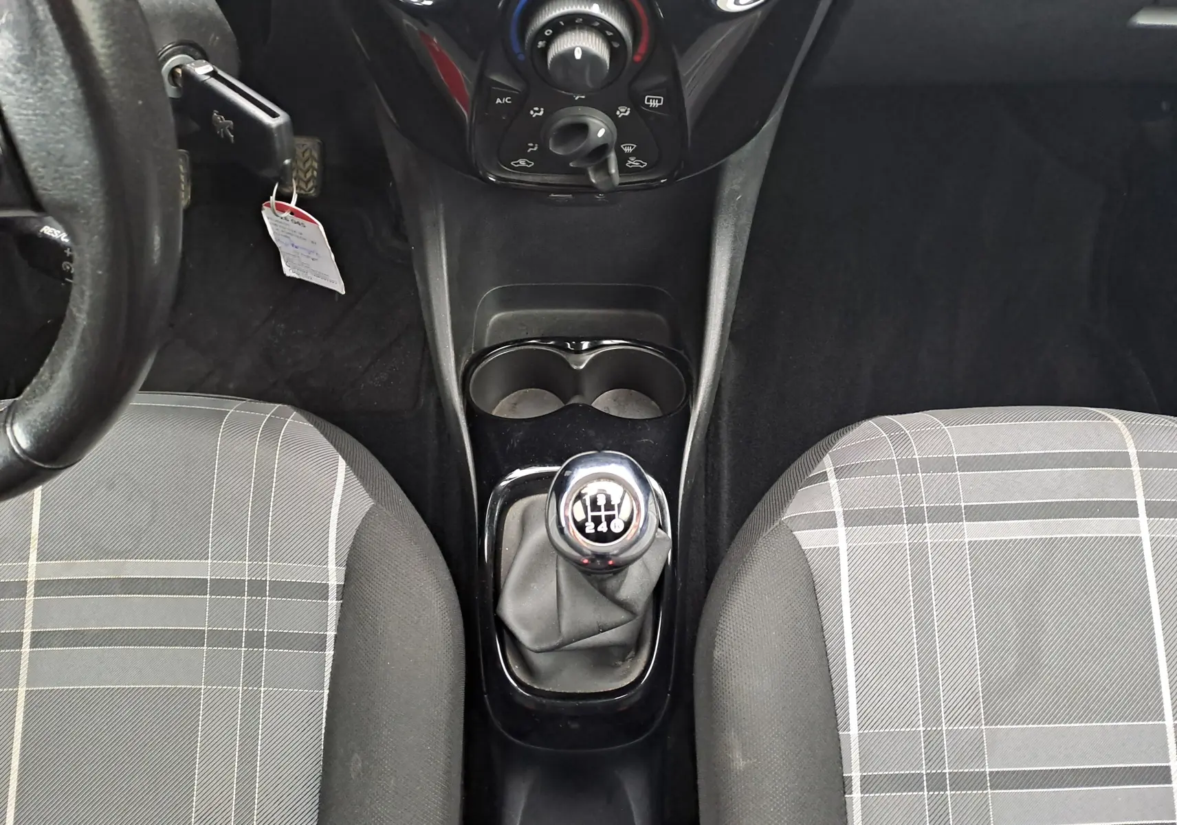 Vue intérieure centrée sur la console centrale d'une Peugeot 108 bleue, montrant levier de vitesses manuel et sièges à motif rayé.