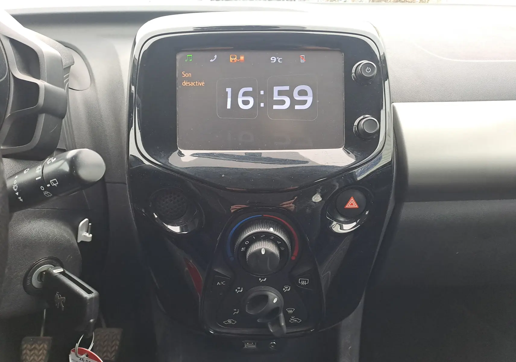 Vue rapprochée du tableau de bord central noir brillant de la Peugeot 108 2016 avec écran digital et commandes climatisation.