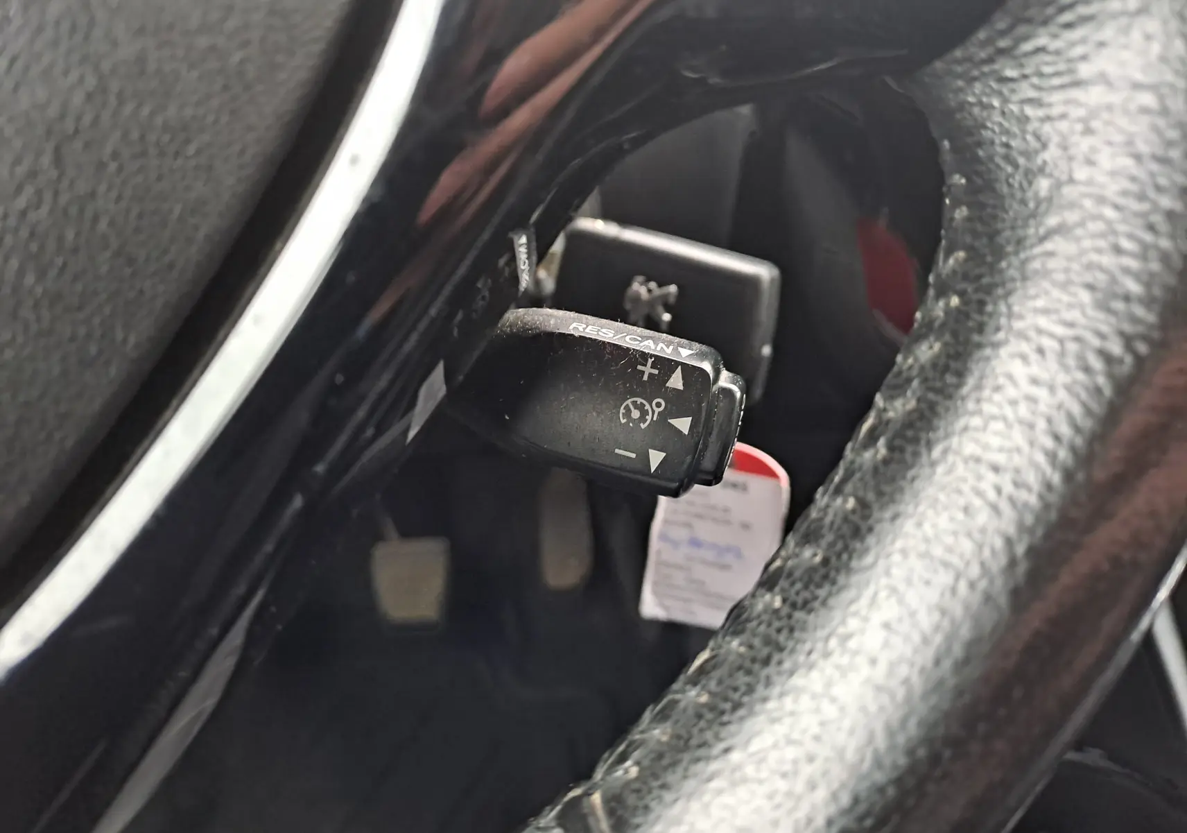 Gros plan sur le levier de régulateur de vitesse derrière le volant noir d'une Peugeot 108 bleu, intérieur visible.