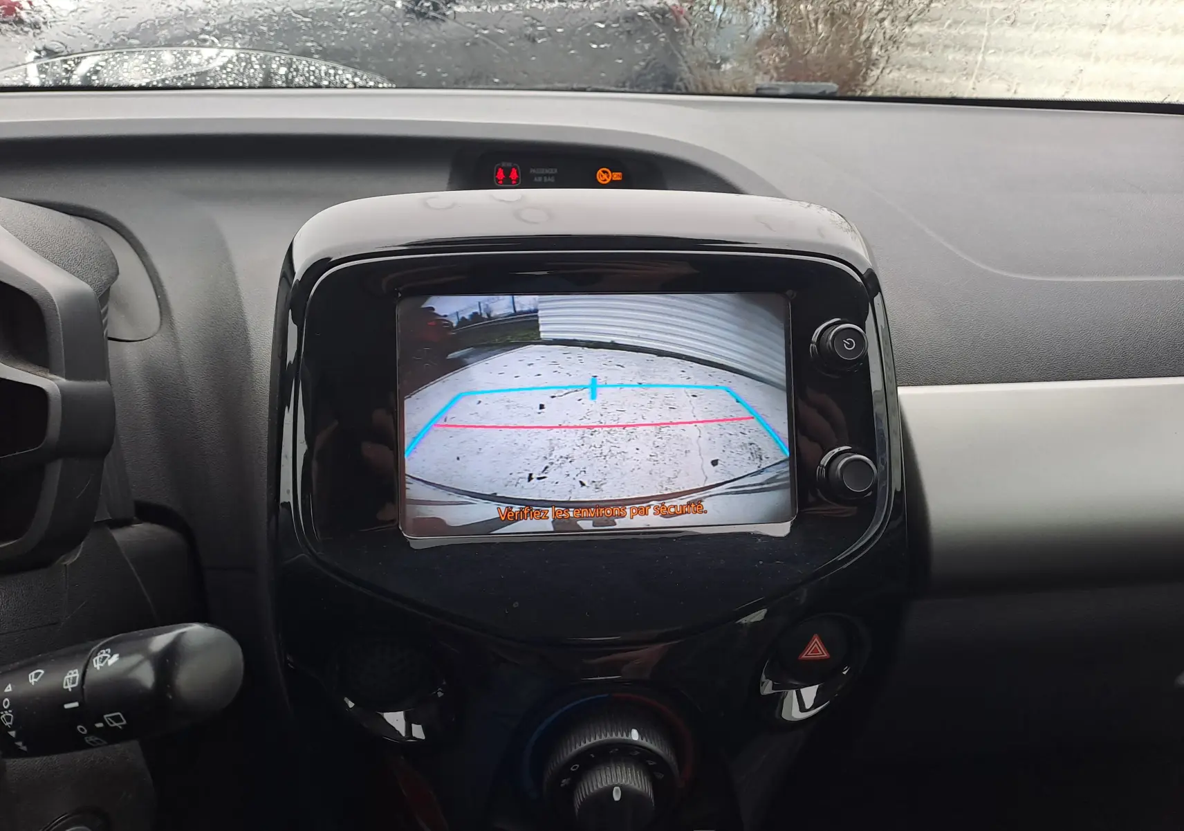 Vue intérieure du tableau de bord de la Peugeot 108 bleu, avec l'écran de la caméra de recul affichant les lignes de guidage.