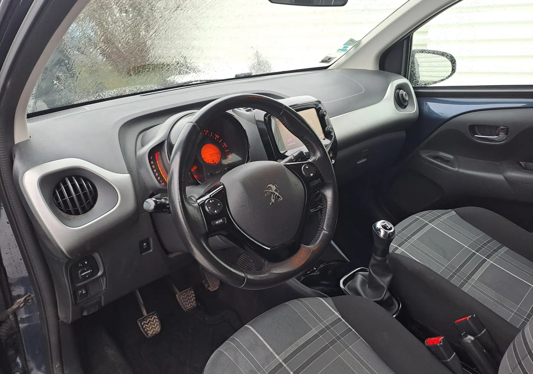 Vue intérieure côté conducteur de la Peugeot 108 bleue, montrant le volant, tableau de bord et levier de vitesse manuel.