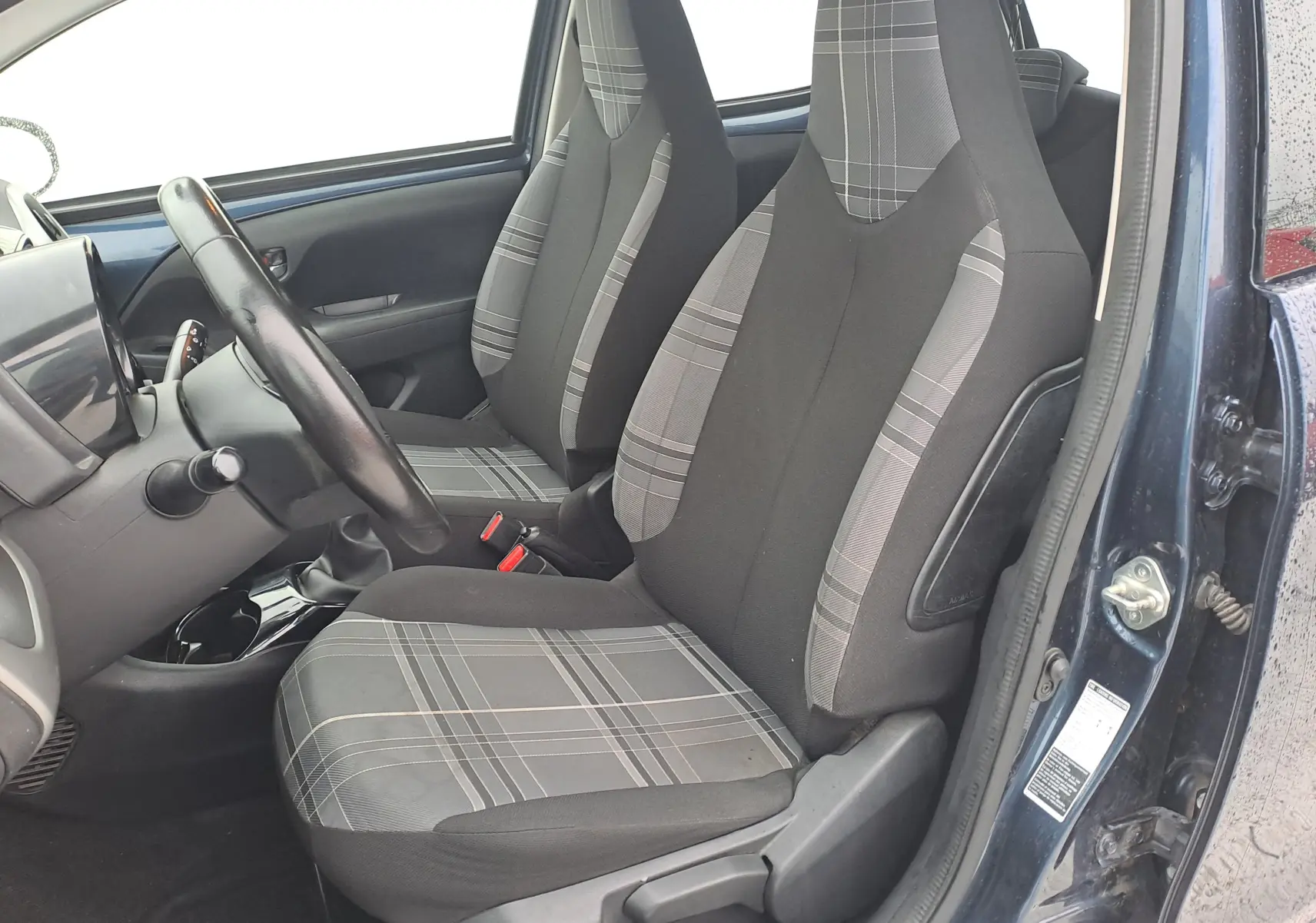 Vue intérieure côté conducteur de la Peugeot 108 bleue, mettant en valeur les sièges tissu à motifs gris et noirs.