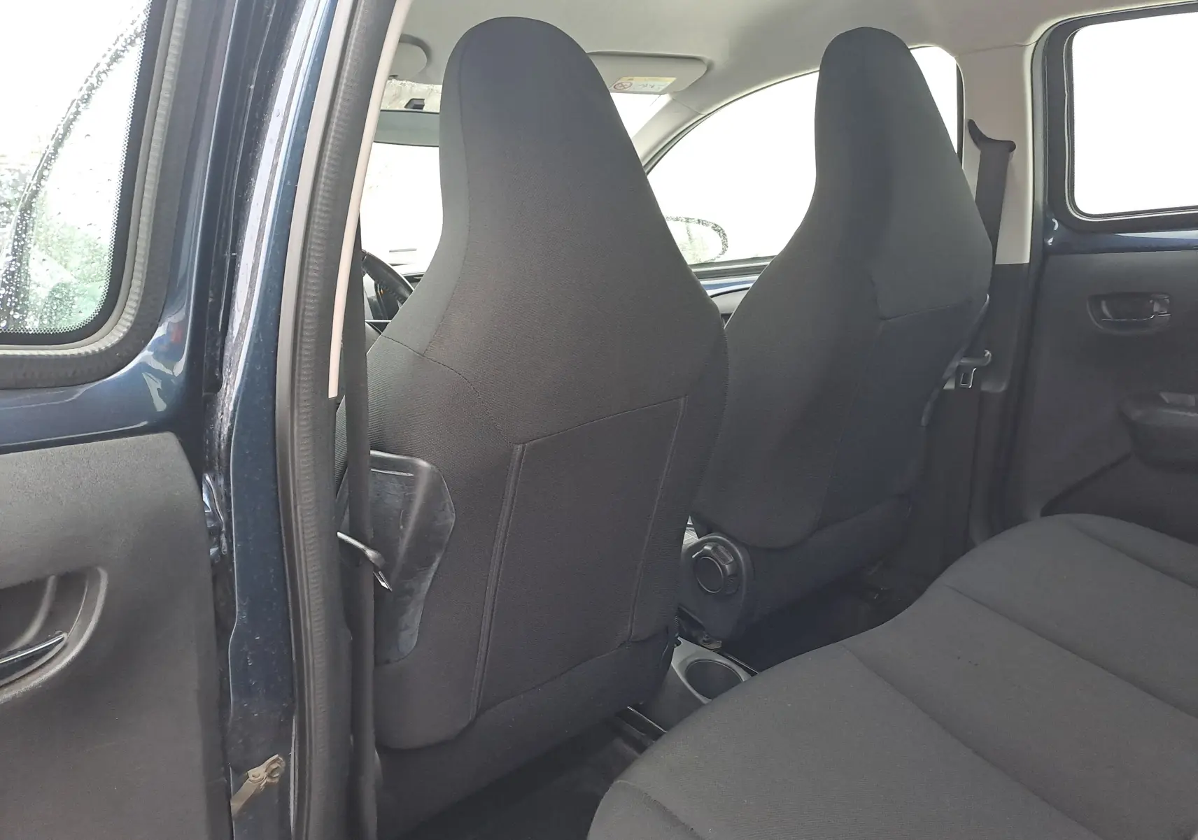 Vue intérieure arrière côté gauche montrant les sièges avant noirs et la portière bleue d'une Peugeot 108 2016.