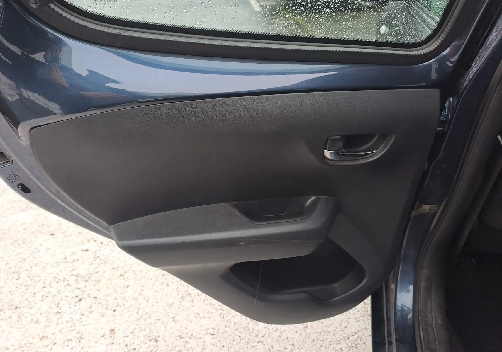 Vue intérieure de la porte arrière gauche d'une Peugeot 108 bleu 2016, avec poignée et panneau noir simple.