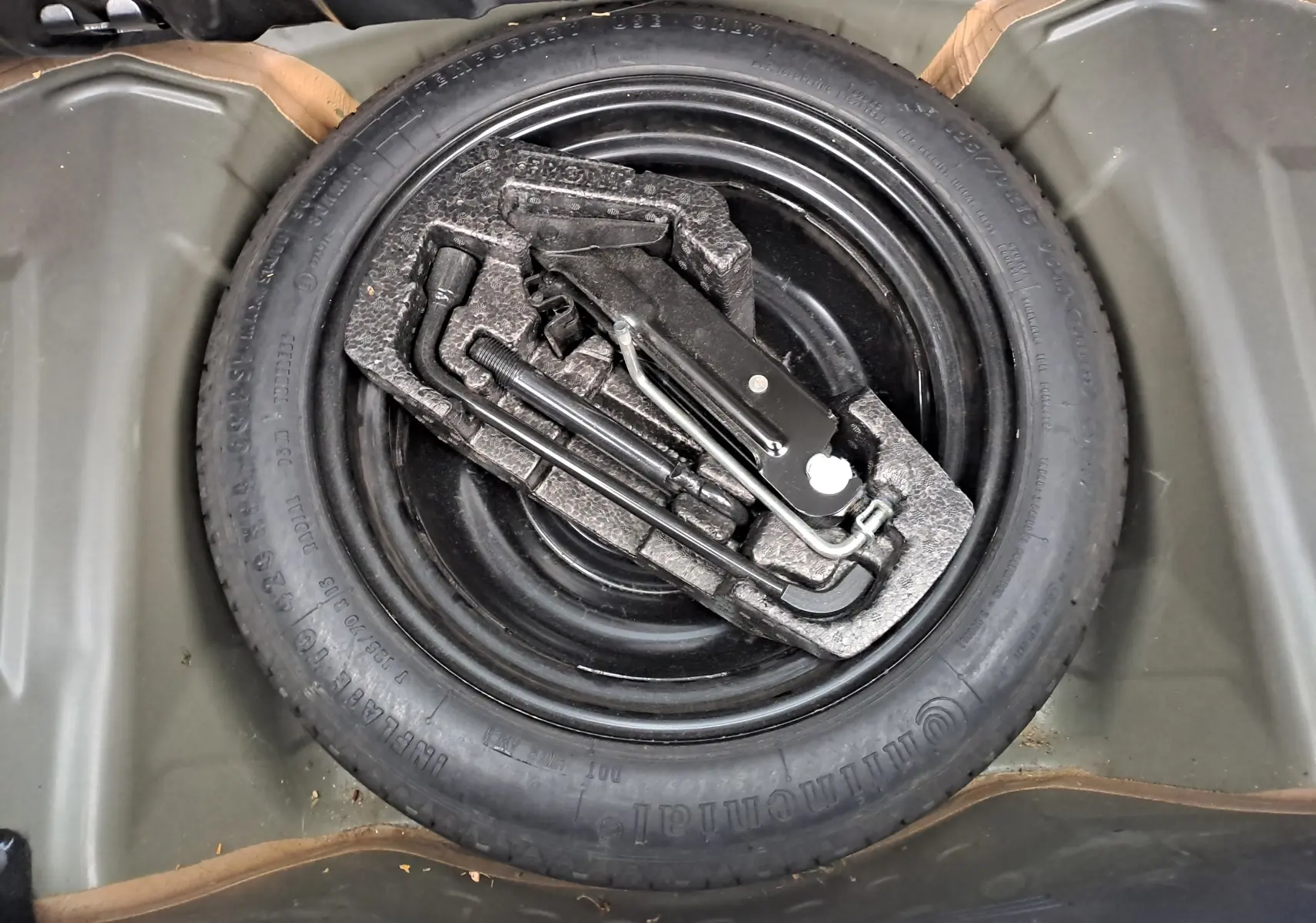 Gros plan sur la roue de secours noire et les outils de bord dans le coffre d'une Peugeot 108 bleue de 2016.