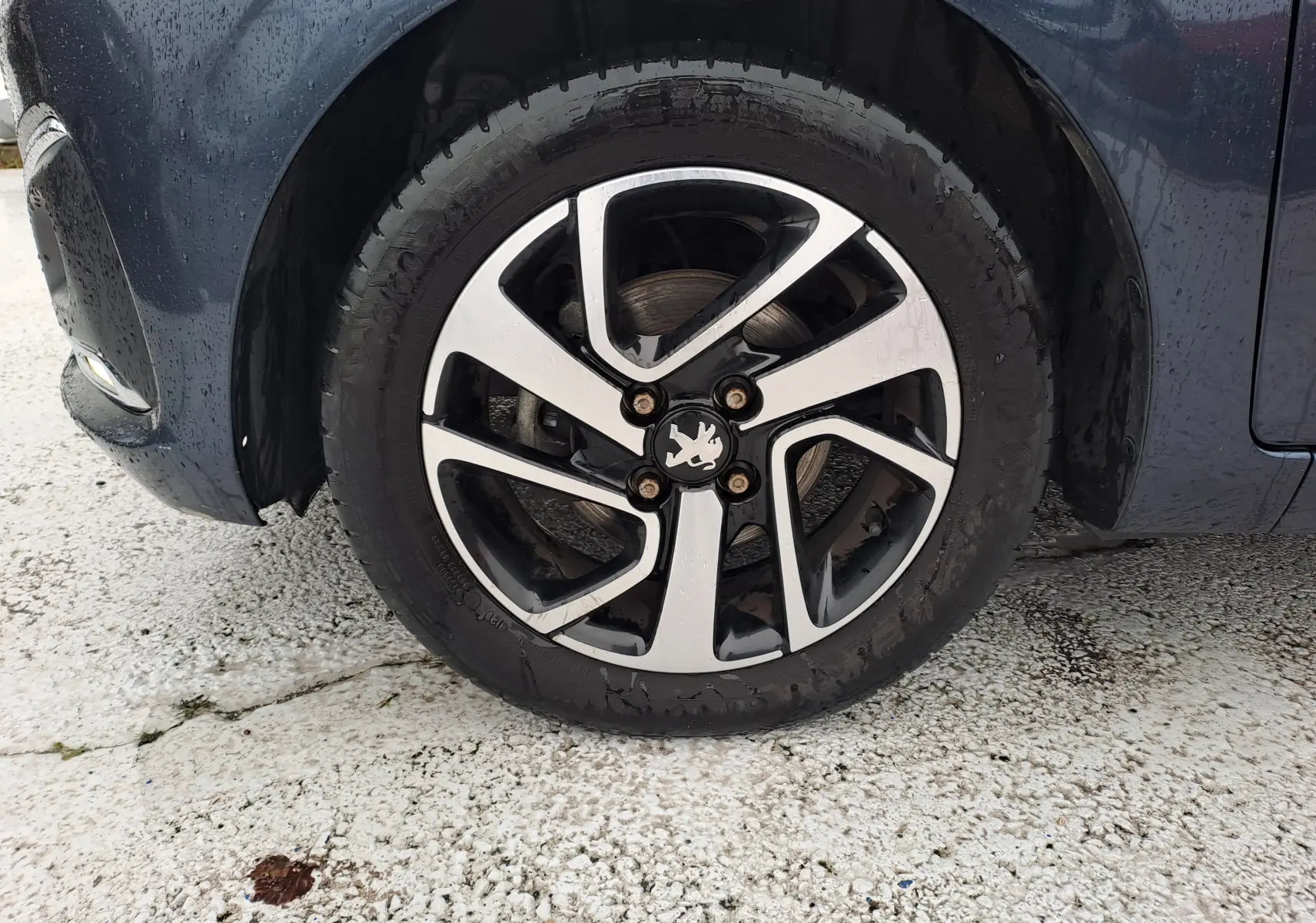Gros plan sur la roue avant gauche d'une Peugeot 108 bleu marine avec jante alliage bicolore et logo lion central.
