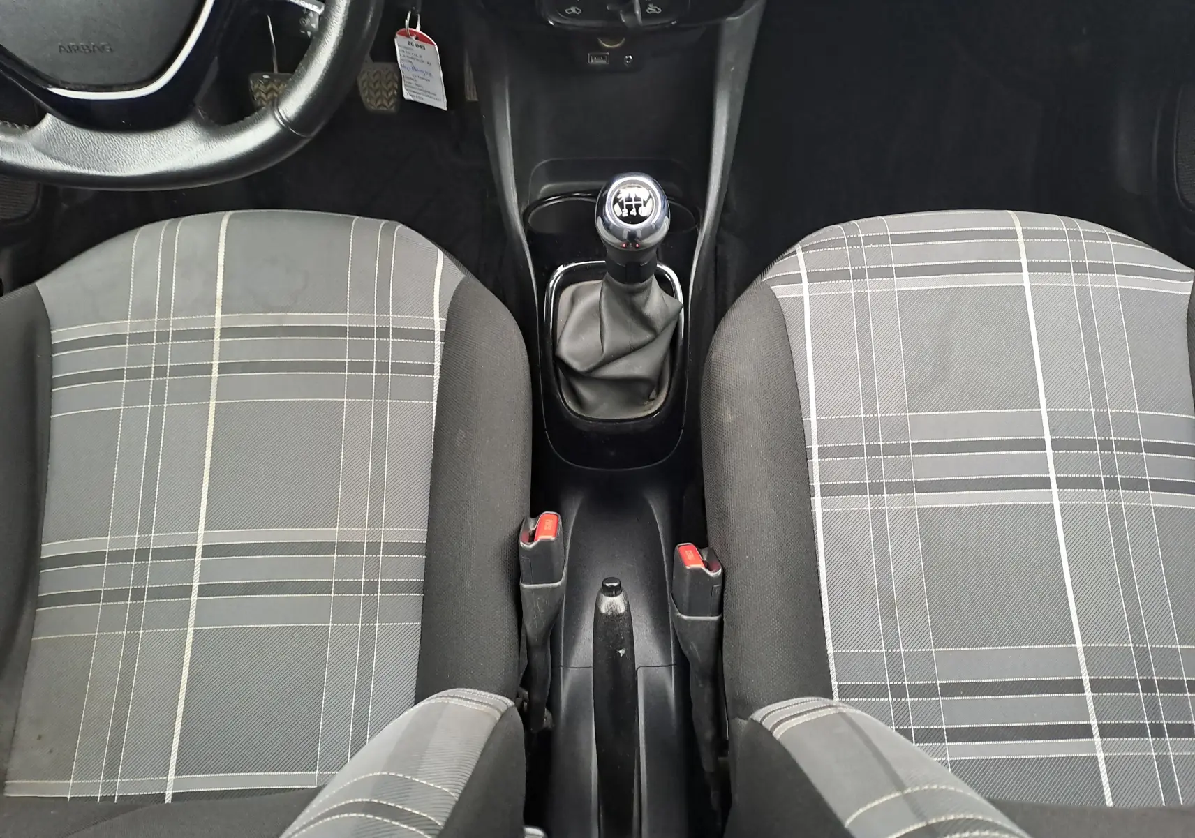 Vue intérieure centrée sur la console centrale et la boîte manuelle de la Peugeot 108 avec sièges avant gris à motif à carreaux.