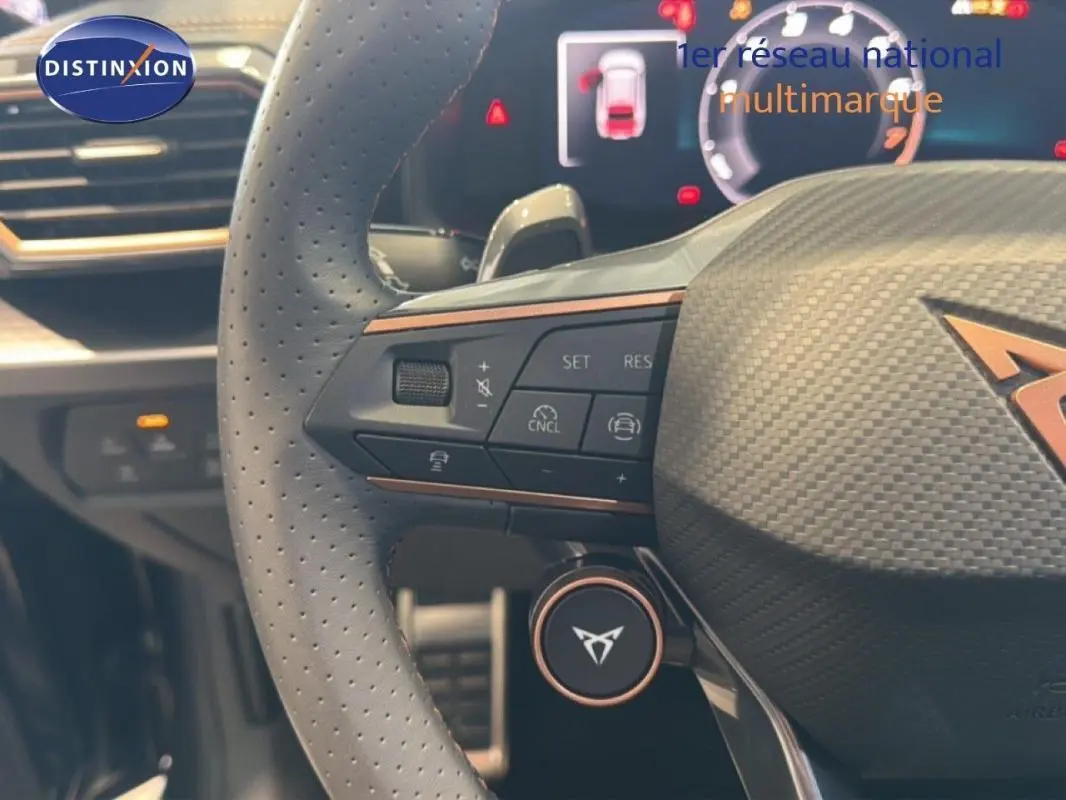 Gros plan sur le volant cuir perforé gris du CUPRA Leon 2025 avec commandes intégrées et logo distinctif cuivre.