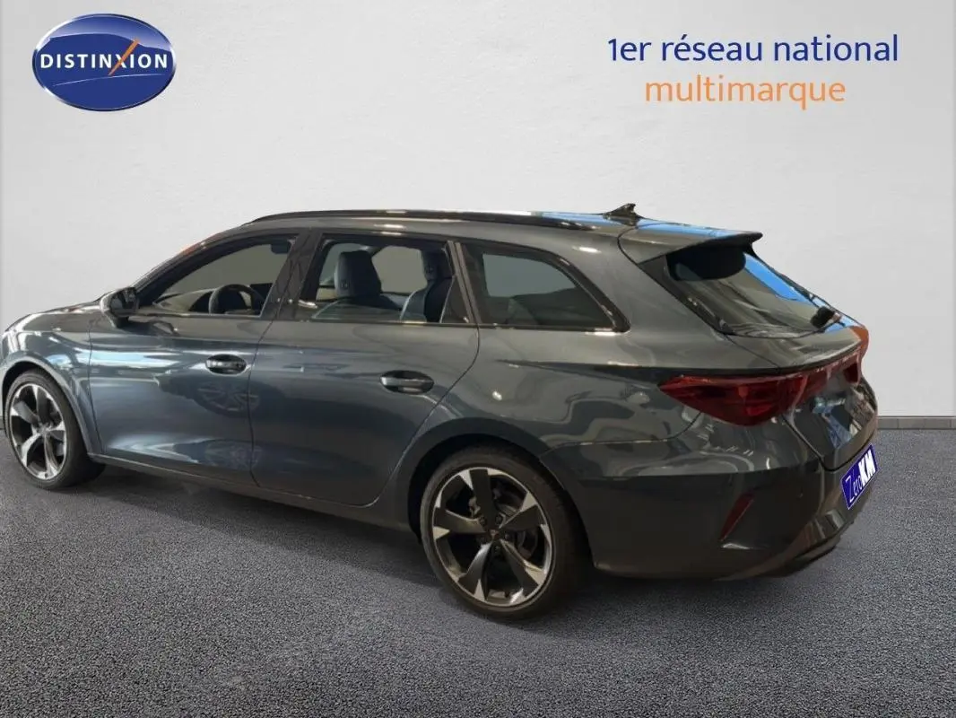 Vue 3/4 arrière droite d'une CUPRA Leon ST gris métallisé avec barres de toit et jantes aluminium distinctives.