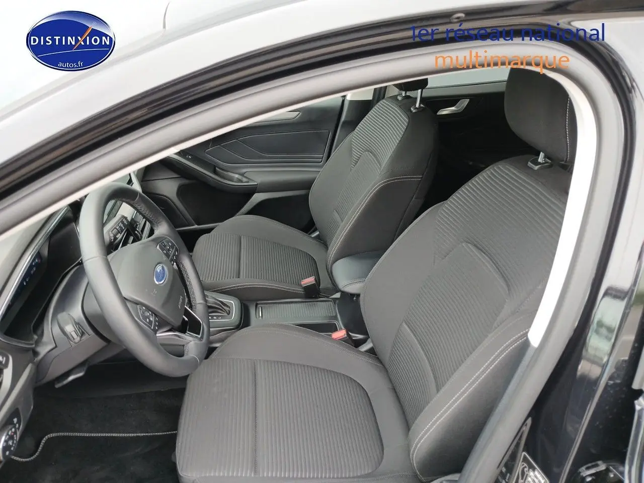 Vue intérieure côté conducteur de la Ford Focus 2024 noir Agate, montrant sièges tissu et volant multifonction cuir.