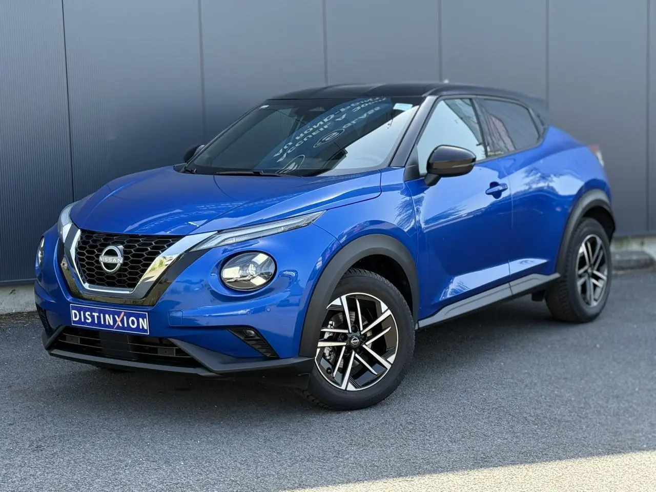 Vue 3/4 avant droite du Nissan Juke 2025 bleu magnétique avec toit noir et jantes alliage 17 pouces diamantées.