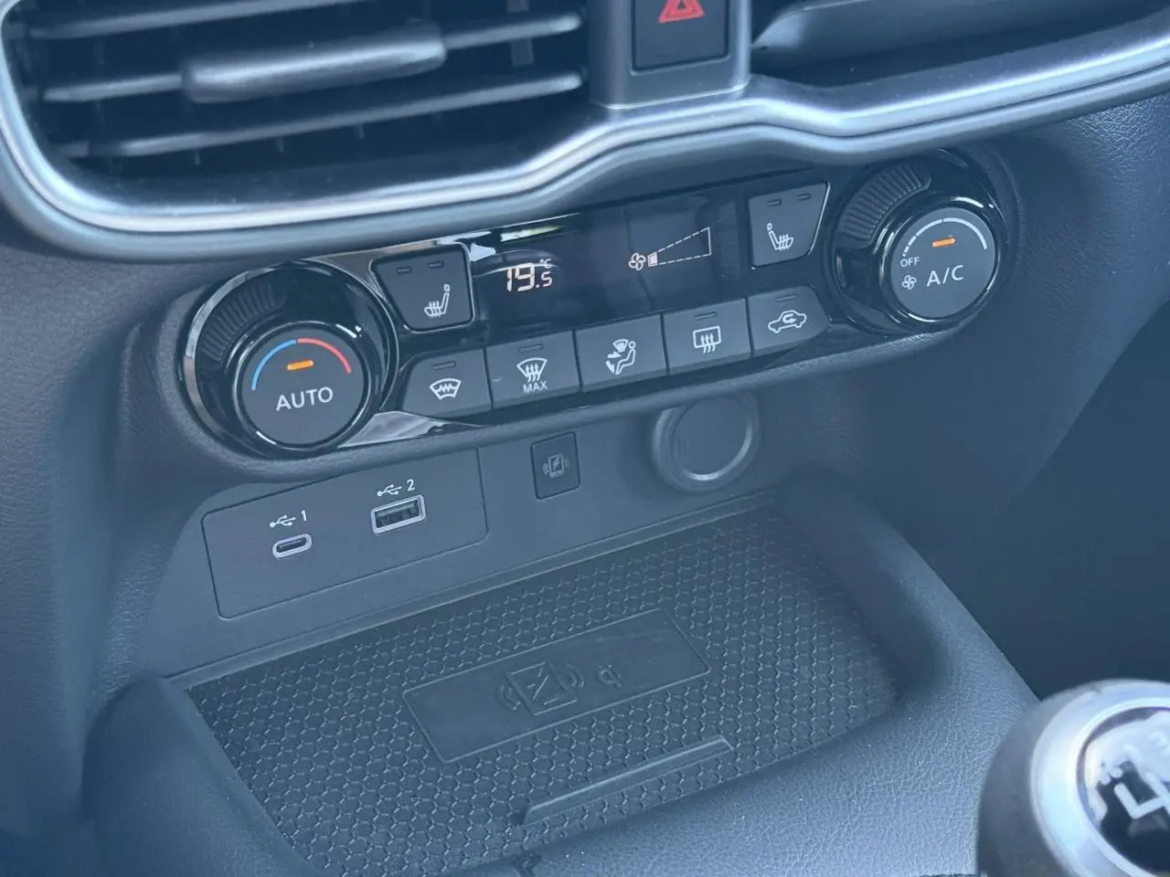 Détail de la console centrale du Nissan Juke 2025, montrant les commandes de climatisation et les ports USB avec recharge sans fil.