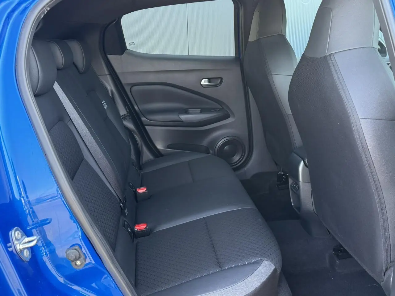 Vue intérieure arrière côté gauche du Nissan Juke 2025 bleu magnétique avec banquette tissu noir et ceintures grises.
