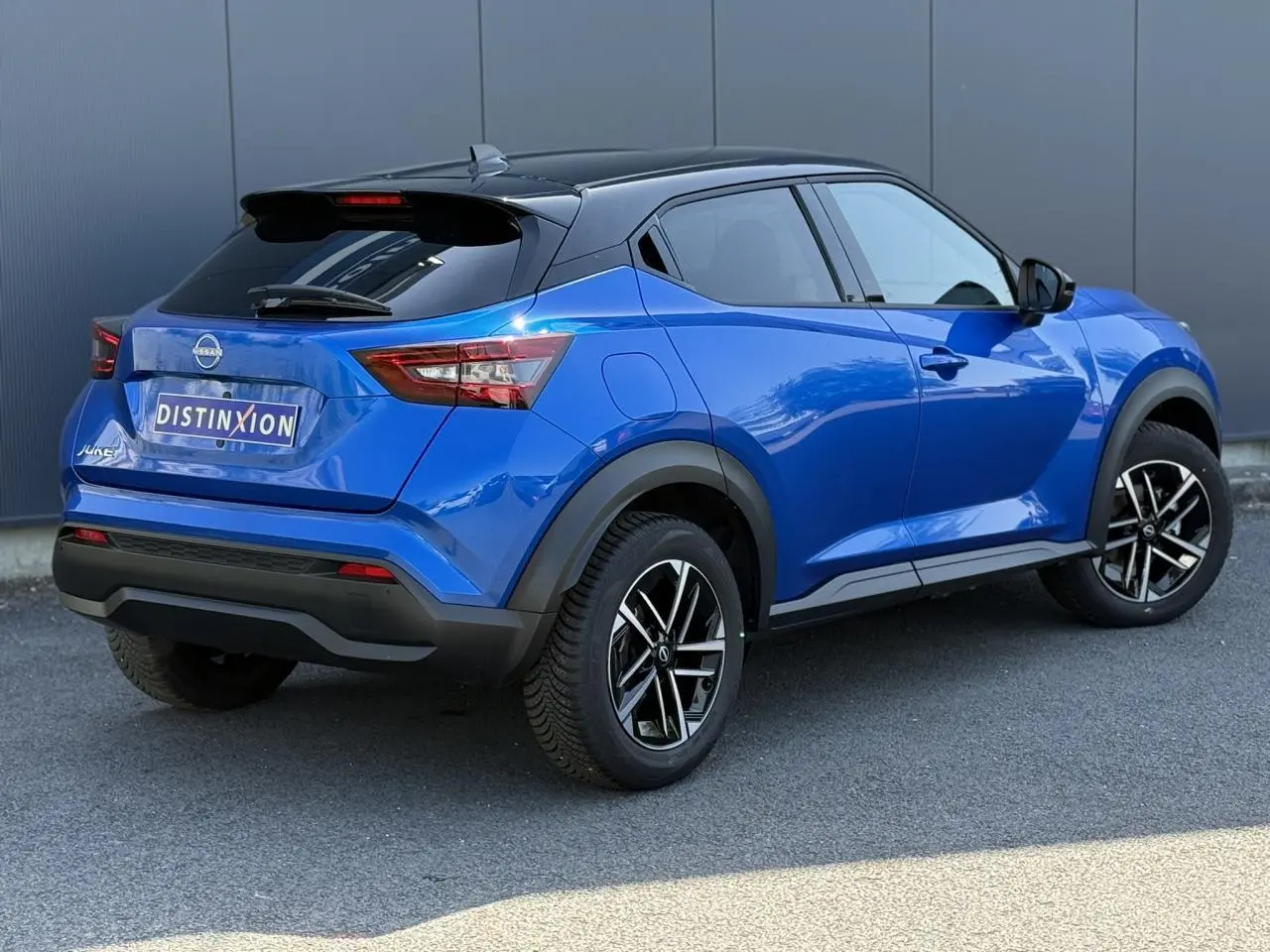 Nissan Juke 2025 bleu magnétique et toit noir, vue 3/4 arrière côté gauche avec jantes alliage 17 pouces.