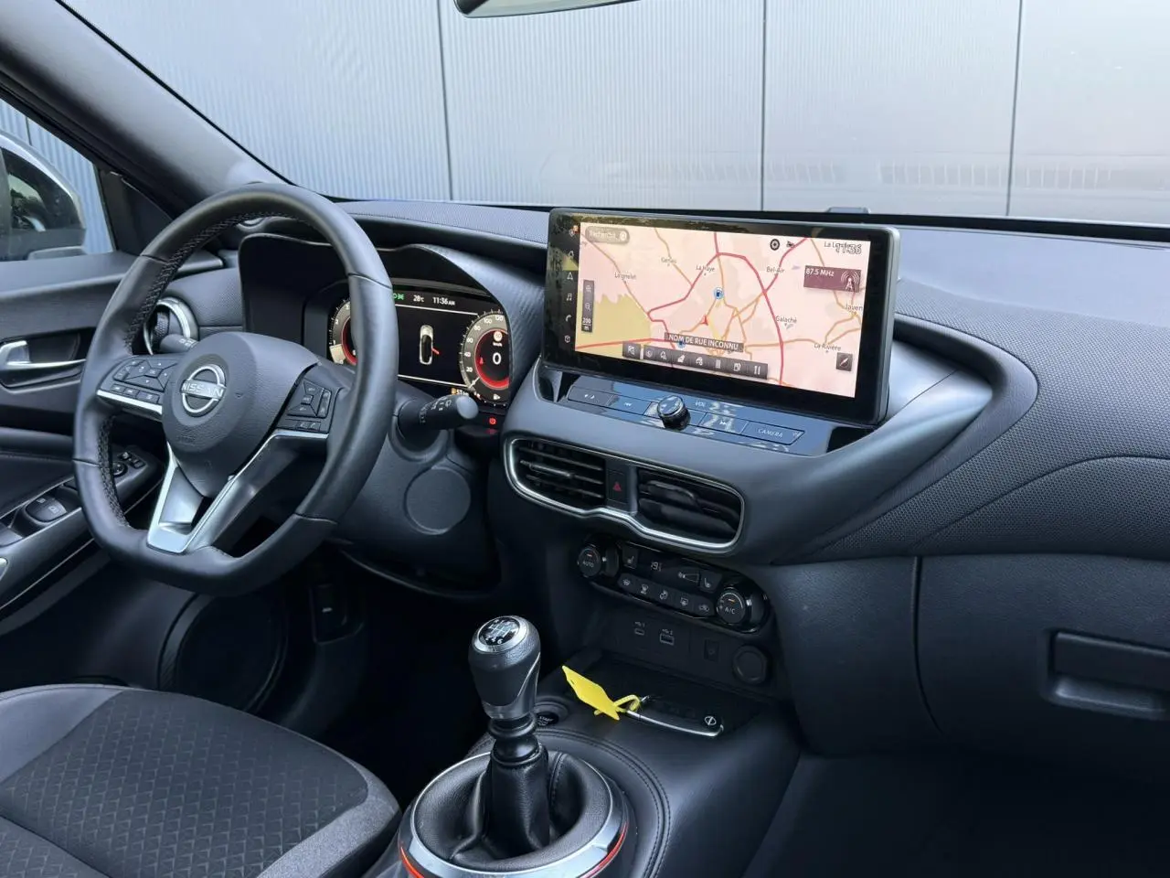 Vue intérieure côté conducteur du Nissan Juke 2025, tableau de bord noir avec écran tactile GPS et levier de vitesse manuel.