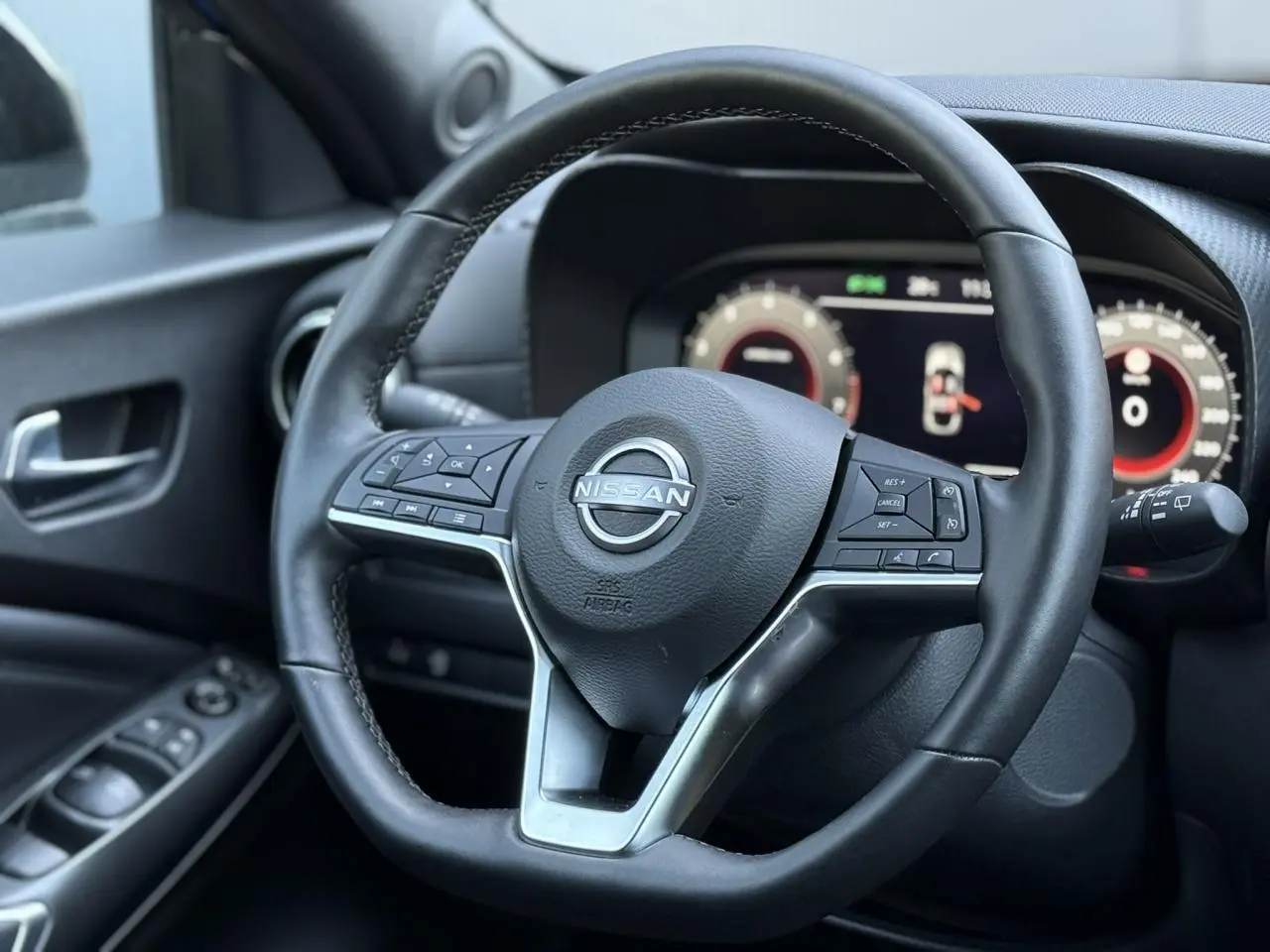 Gros plan sur le volant en cuir noir du Nissan Juke 2025 avec commandes intégrées et tableau de bord digital en arrière-plan.