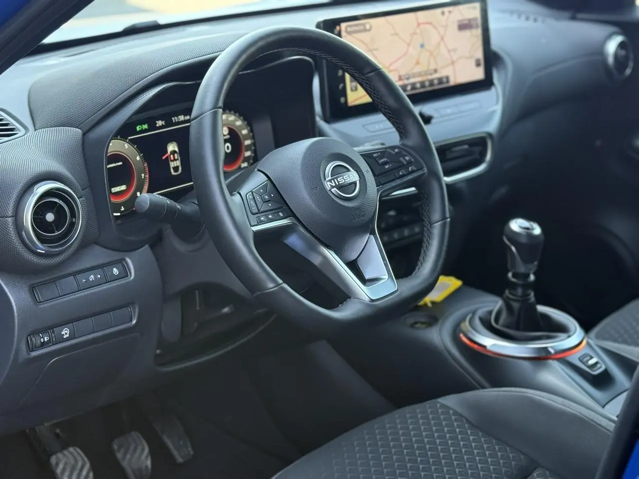 Vue intérieure côté conducteur du Nissan Juke 2025 bleu magnétique, volant cuir, écran tactile GPS et boîte manuelle.